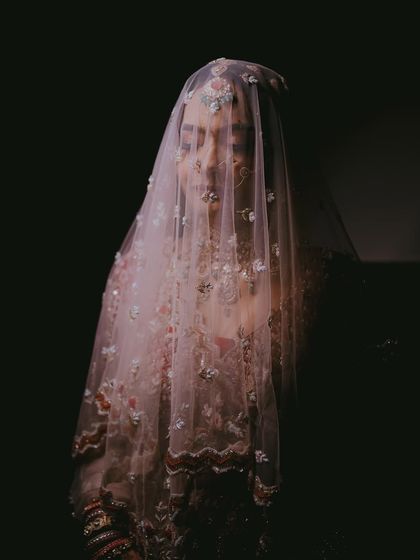 An artistic and mysterious bridal portrait, with the bride's face partially obscured by her delicate, embroidered veil.