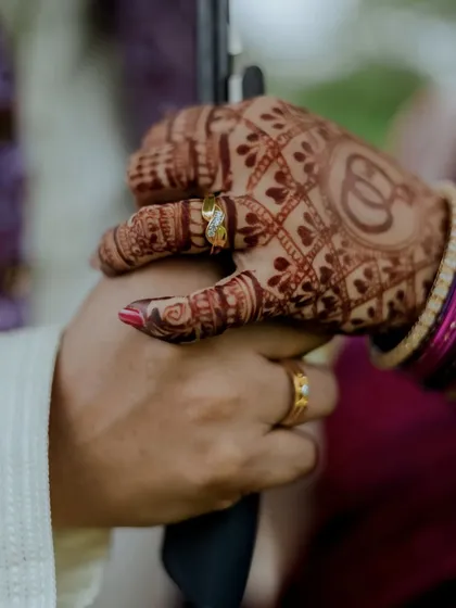 A close-up on the couple's hands, showing the engagement rings and the bride's beautiful henna design with the 'Om' symbol.
