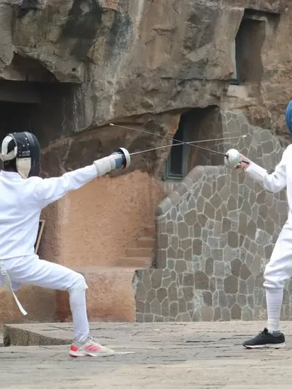 Two of our fencers engage in a practice bout against the stunning backdrop of the Aurangabad Caves. This image shows a classic fencing exchange, with one athlete extending in a lunge while the other prepares a defensive move.