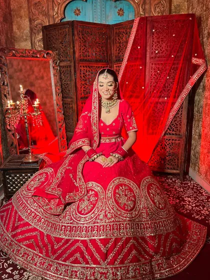 A seated portrait of a bride in a stunning red lehenga, showcasing the intricate details of the skirt and the beautiful bridal jewelry.