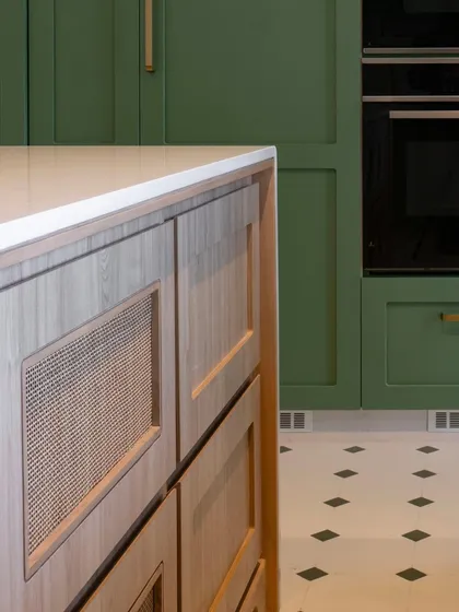 A close-up of the island in the soft green kitchen, showing the detail of the cane-fronted drawers. This natural material adds a beautiful texture that contrasts with the smooth, painted finish of the surrounding cabinetry.