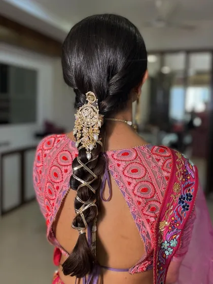 A sleek and intricate braid wrapped with golden thread and topped with a heavy, traditional piece of jewelry. This is a statement look for a bride who wants her hair to be a major part of her ensemble.