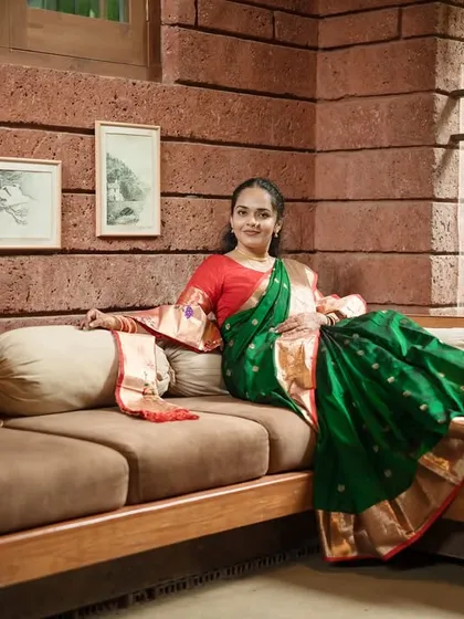 A full-length portrait showing the bride relaxing on a sofa. This shot showcases the beautiful drape of her saree and her comfortable, graceful presence.