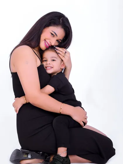 A mother and her child share a warm hug, both smiling brightly for the camera. This simple studio portrait beautifully captures the loving bond between them.