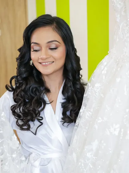 A moment of admiration as the bride looks at her wedding gown. Her makeup is soft and shimmery, with beautiful curls ready to be styled.