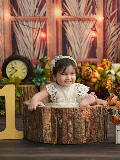 A smiling baby girl in a rustic log tub. The warm lighting and wooden elements create a cozy and enchanting atmosphere for her first birthday photos.