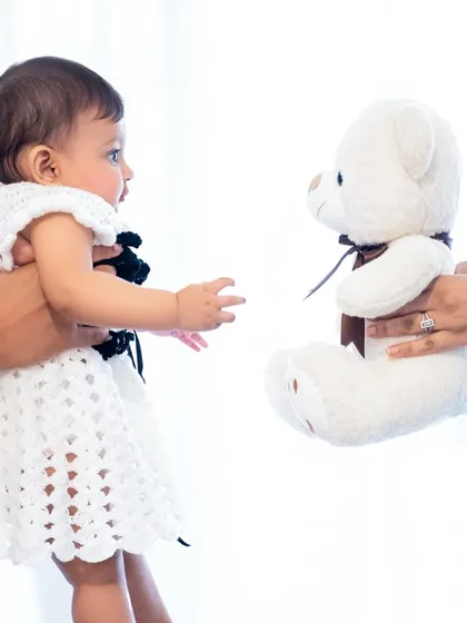 A side profile of the baby reaching for her teddy bear. The high-key lighting and white background create a clean, modern, and airy feel for this baby portrait.