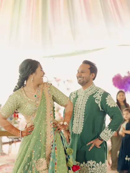 A candid moment of the couple during their Mehendi performance. The green and pastel outfits blend beautifully with the daytime decor.