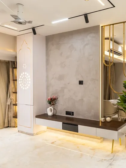 This open-concept living area balances form and function. A calming palette of muted neutrals meets gleaming gold accents and warm lighting. The graceful brass partition and sculptural lighting bring depth and drama, while indoor greens add a touch of serenity.