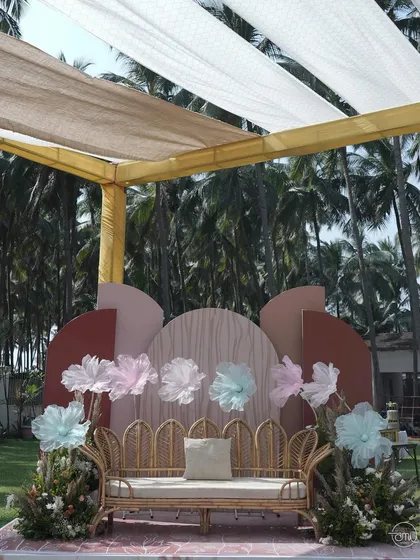 A chic and bohemian seating area for a wedding carnival. The rattan sofa, oversized paper flowers, and a backdrop of earthy tones created a stylish and comfortable spot for guests to relax.