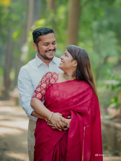 An embrace filled with smiles. The groom holds the bride from behind as they look at each other with pure joy, surrounded by the greenery of the temple grounds.