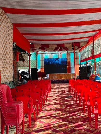 A pandal setup for a community event. The arrangement includes seating for the audience, a stage for performances or ceremonies, and a large LED screen at the back for visuals.