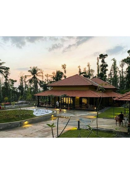 The modernized estate bungalow in Sakleshpur at sunset. The design respects the traditional sloping roof architecture while opening up the structure to the surrounding coconut groves and lush landscape for a perfect indoor outdoor living experience.
