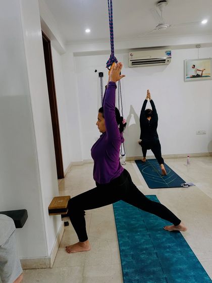 A student uses the yoga wall ropes to find more lift and openness in Virabhadrasana I (Warrior I). This helps to deepen the backbend and stretch the hip flexors safely.