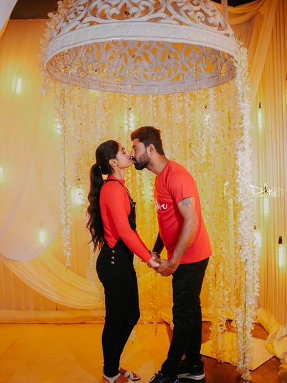 An intimate kiss under a beautifully decorated canopy with hanging flowers and lights.