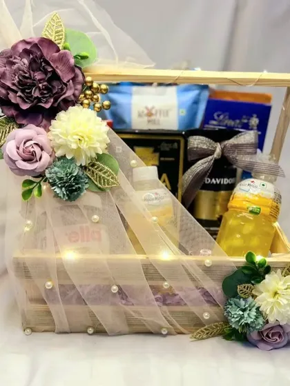 This trousseau hamper, packed in a rustic wooden crate and wrapped in delicate net with floral accents, is perfect for gifting gourmet food items or skincare essentials to the new couple.