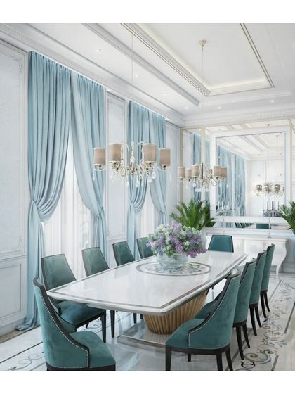 This elegant dining room showcases custom drapery in a soft powder blue, complementing the upholstered dining chairs. The design balances classical elements like wall paneling with modern lighting for a transitional luxury aesthetic.