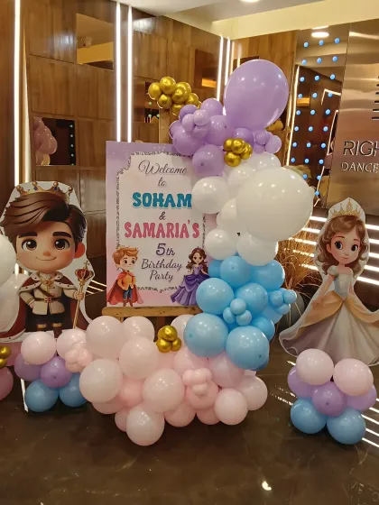 A personalized welcome stand for a royal-themed 5th birthday party. This entry decor features princess and prince cutouts and a balloon arrangement, greeting guests to Soham and Samaria's celebration.