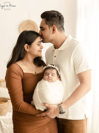 A beautiful portrait of new parents holding their swaddled baby. The father's kiss on the mother's head adds a layer of romance and partnership.