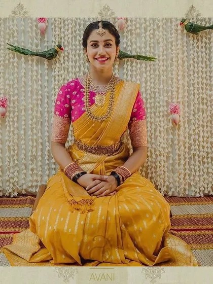 A full-length view of the bride in her yellow and pink attire, seated in a traditional setting. The custom blouse adds a touch of modern craftsmanship to the look.