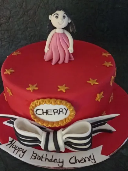 A simple yet charming red fondant cake with a cute girl topper and a black and white striped bow. The gold stars add a touch of sparkle.