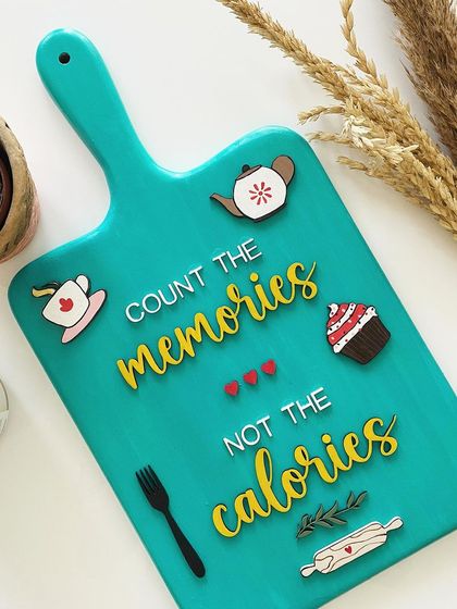 A fun piece for your kitchen wall! This decorative cutting board reminds us to "Count the memories, not the calories." The 3D elements like the cupcake and teapot add a playful touch.
