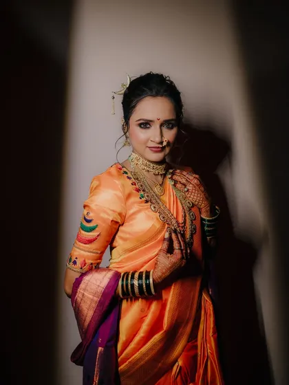 A full-length bridal portrait using dramatic lighting to create a spotlight effect, making the bride and her stunning orange saree the absolute focus.