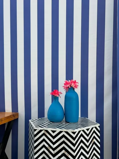 A minimalist yet striking detail from the Uttarayan event. Two blue vases with simple pink flowers sit on a chevron-patterned table against a bold blue-and-white striped wall, showcasing our eye for graphic compositions.