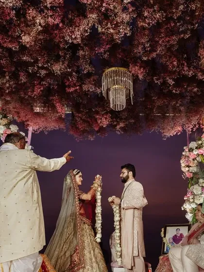 The couple shares a look during their Varmala ceremony. The twilight sky and the stunning floral decor provide a romantic and dramatic backdrop for this pivotal moment.