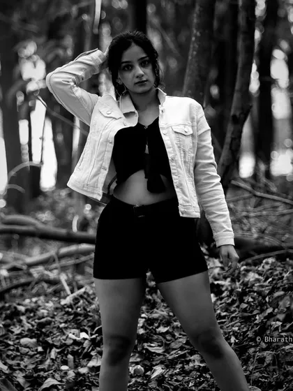 A full-body shot of a model in a denim jacket and shorts, set in a wooded area. The black and white conversion enhances the textures of the foliage and the outfit.