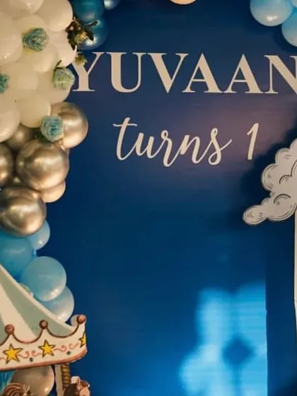 A close-up of the royal blue first birthday theme, showing the custom 'Yuvaan turns 1' signage and cloud cutout.