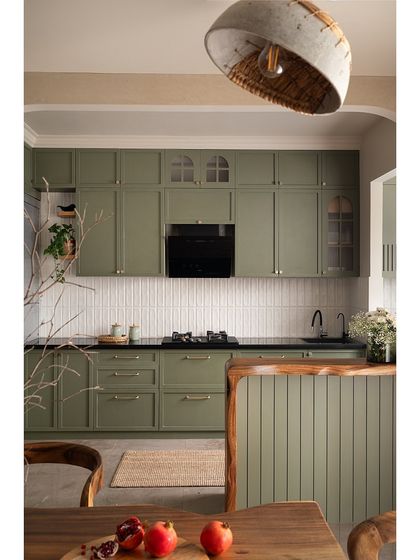 A view from the dining area into the kitchen, highlighting the live-edge breakfast counter with grooved details. The olive green cabinets and white subway tiles create a timeless contrast.