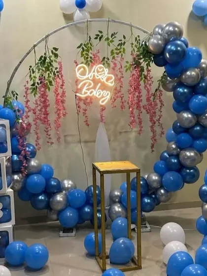 A stylish 'Oh Baby' shower for a baby boy. A circular frame is decorated with blue and silver balloons and hanging floral elements, complemented by 'BABY' blocks.