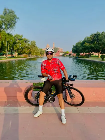 A rider in a striking red floral jersey takes a break with his bike by the water at Vijay Chowk.