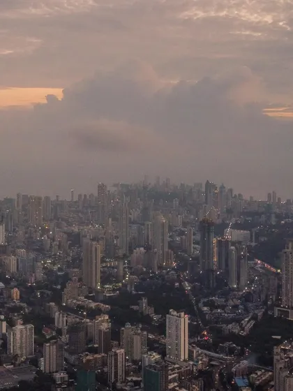 A drone's view looking down on the dense urban fabric of Mumbai, with clouds gathering over the city.