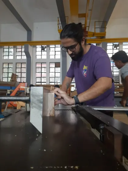 A student carefully guides a piece of wood through the table saw, a versatile machine used for ripping, cross-cutting, and creating joinery.