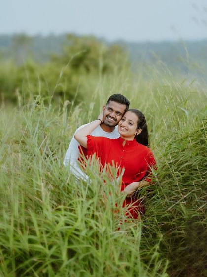 A cozy embrace amidst tall green grass. The foliage creates a natural frame, drawing focus to the couple's happy expressions.