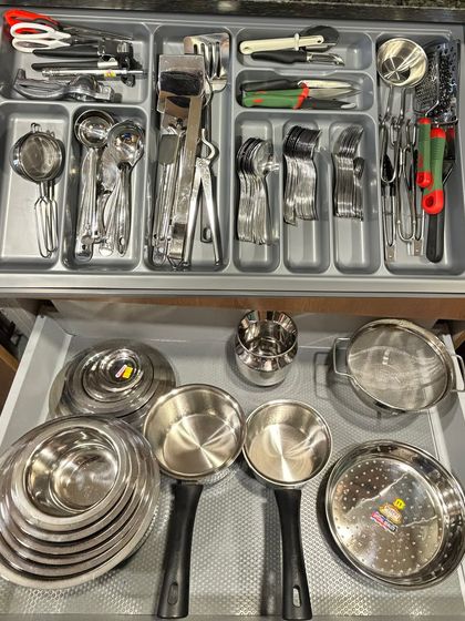 A complete drawer system for an Indian kitchen. The top drawer is for cutlery and tools, while the bottom holds steel tiffins, bowls, and serving spoons, all neatly arranged.
