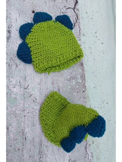 A detailed product shot of my handmade dinosaur outfit. You can see the texture of the yarn and the construction of the blue spikes on the lime green hat and diaper cover.