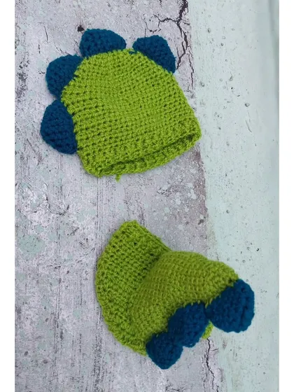 A detailed product shot of my handmade dinosaur outfit. You can see the texture of the yarn and the construction of the blue spikes on the lime green hat and diaper cover.