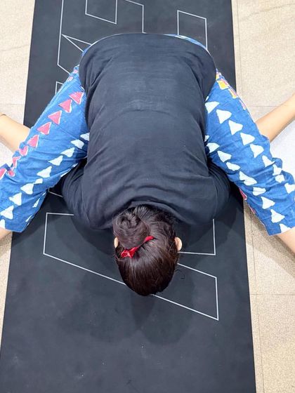 A student in Kurmasana (Tortoise Pose), a deep forward fold that symbolizes drawing one's senses inward. This pose requires patience and open hips.