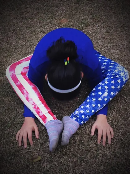 A young girl demonstrates incredible flexibility in a forward bend pose. Children are often naturally flexible, and yoga helps them maintain it.