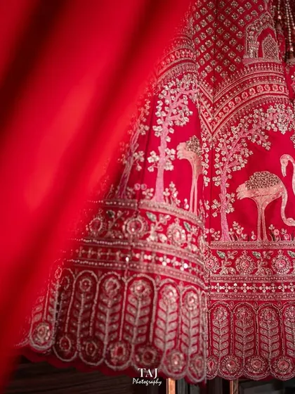 A creative detail shot of the bridal lehenga, using a foreground element to draw the eye to the intricate embroidery. This technique adds depth and an artistic touch to wedding detail photography.