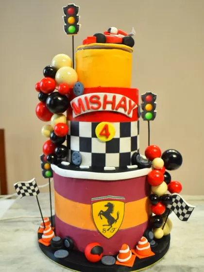 A massive, multi-tiered Ferrari race car-themed cake for a 4th birthday. This complex structure features checkered flags, traffic lights, and the iconic Ferrari logo, making it a dream cake for a young racing fan.