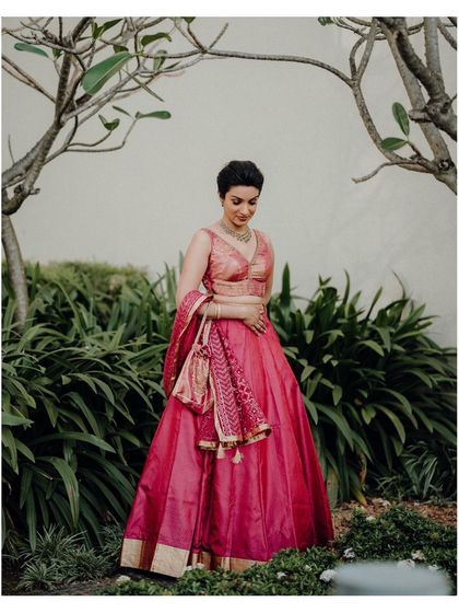A full-length portrait of Jisha in her elegant pink lehenga, set in a beautiful garden.