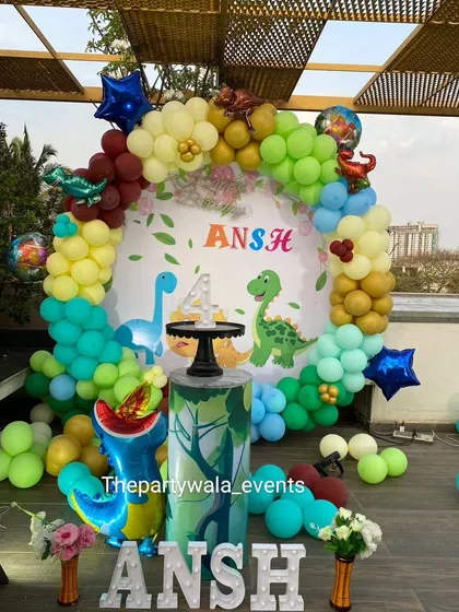 Roar! A colorful dinosaur theme for a 4th birthday party. This outdoor setup includes a multi-colored balloon arch and cute dinosaur cutouts.