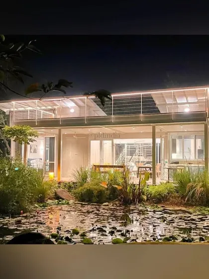 A wide view of the house and pond at night. The combination of interior and exterior lighting creates a stunning reflection on the water's surface, doubling the beauty of the scene.