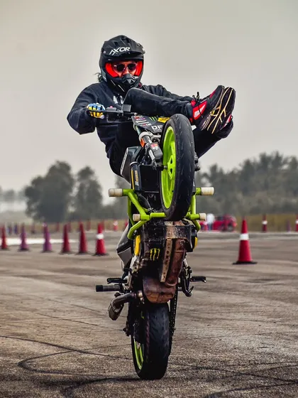 A rider executes a "high chair" wheelie, sitting on the handlebars while the bike is on one wheel. This is an advanced stunt that requires incredible core strength and balance.