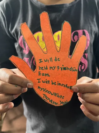 A child proudly displays a craft where they've written down acts of kindness. After our stories, we encourage children to think about how they can apply values like friendship and helping others in their own lives.