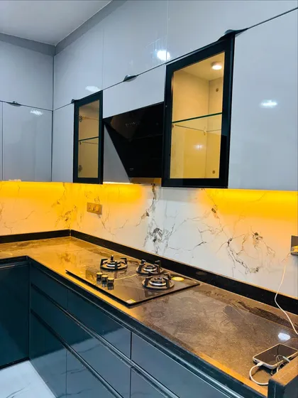 A close-up of a sleek kitchen design with a built-in hob and a modern chimney. The yellow-tinted glass cabinets with internal lighting add a unique, warm accent to the space.